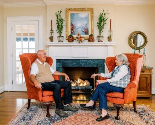 Older couple sitting on orange wingback chairs enjoying a gas fireplace to lower their energy bills.