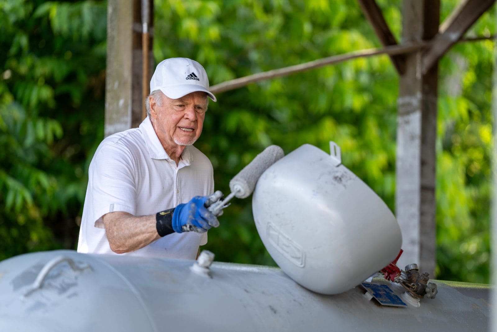 Propane tank being painted by a man in a white hat and a white shirt